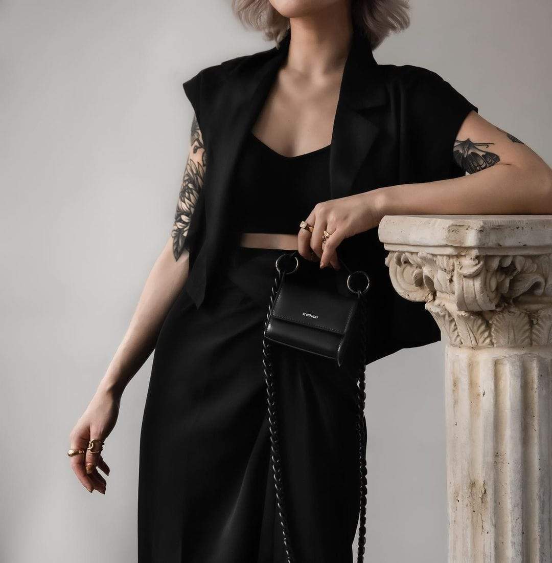 X NIHILO - TRANQUIL MINI SHOULDER BAG - BLACK Held by model with tattoos leaning on Greek column 