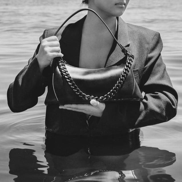 Black and white shot of bag in arms of model wearing suit jack standing in water
