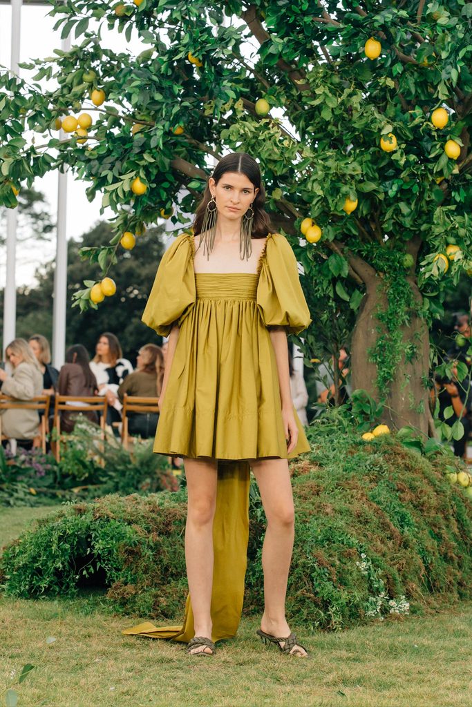 Model wearing AJE - CASABIANCA PUFF SLEEVE MINI DRESS - GREEN In lemon orchard