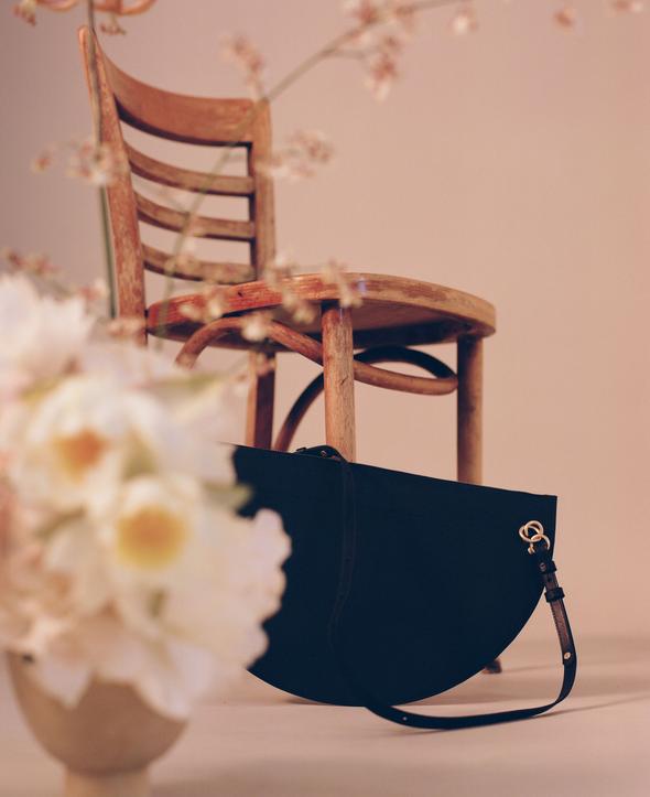 SIMÉTRIE - XL CRESCENT MOON BAG - BLACK Styled amongst chair and flowers