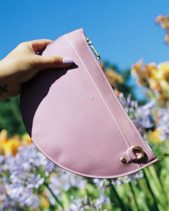 SIMÉTRIE - M CRESCENT MOON BAG - PURPLE Held in front of flowers and blue sky